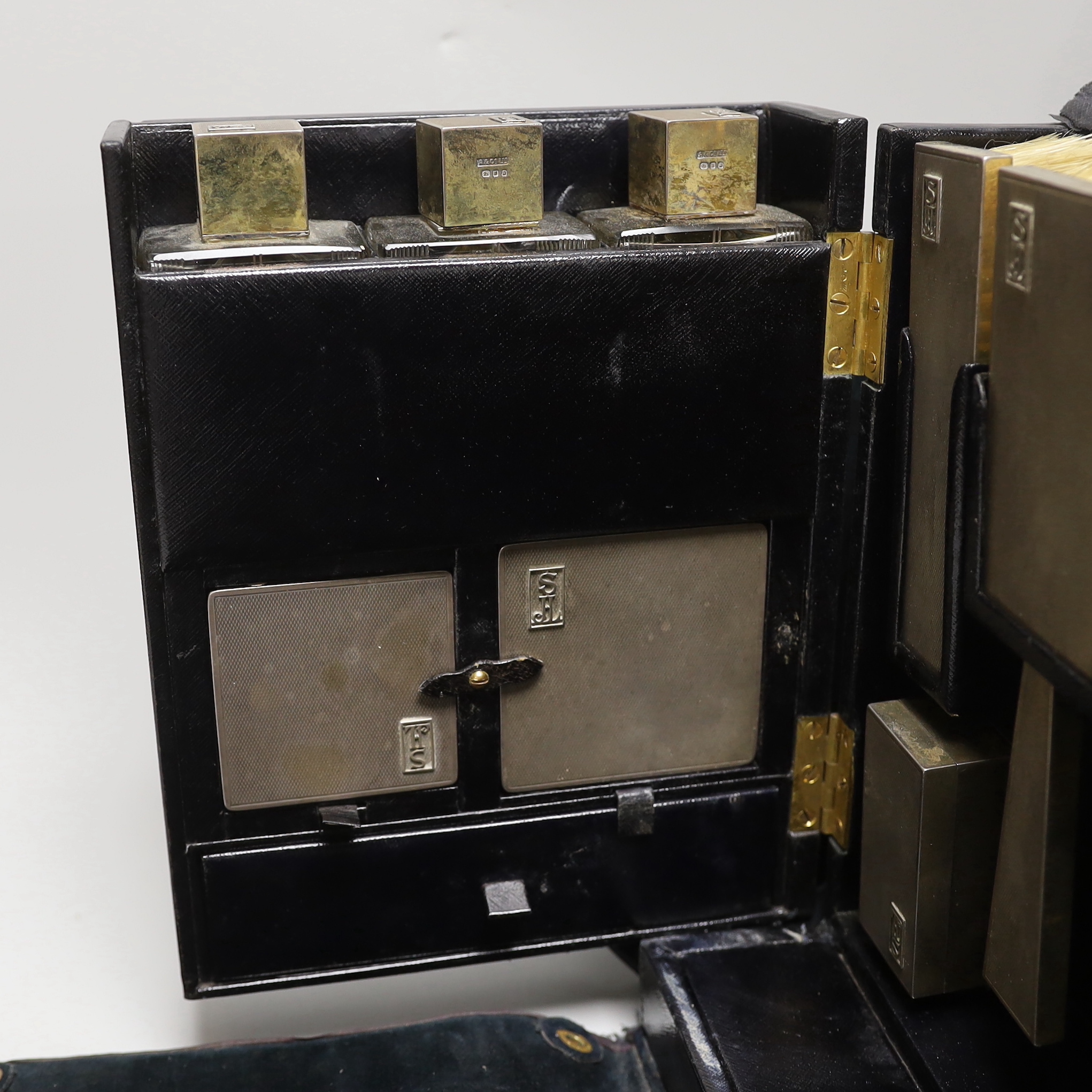 A George VI leather travelling vanity case, containing seventeen monogrammed silver mounted items, including ten mounted glass toilet jars, two boxes, four brushes and a hand mirror, Asprey & Co, London, 1936, case width